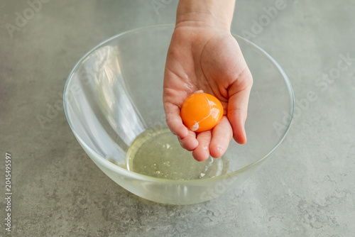 Close-up of a child's hands carefully separating an egg yolk from the egg white using their fingers over a bowl