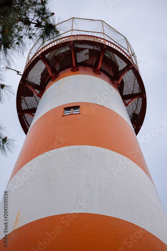Lighthouse stands tall with orange and white stripes under grey sky