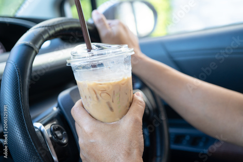 Asian lady holding ice coffee to eat in car, dangerous and risk an accident.