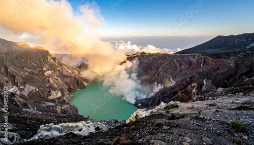 Turquoise lake nestled in a volcanic crater with swirling smoke and rock formations, captured from a high vantage point
