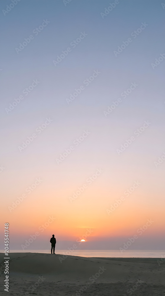 Fototapeta premium Dream and Sunrise for inspirational quote poster theme. Lone figure on a tranquil beach at sunset beneath a vast pastel sky