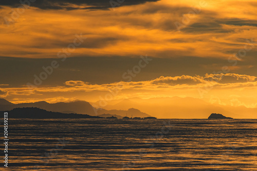Bild auf Leinwand Dramatic Orange Twilight Sky Over Sea and Mountain Silhouettes