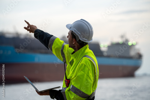 Foto Marine engineer holding a laptop and pointing towards a container ship at a commercial port terminal