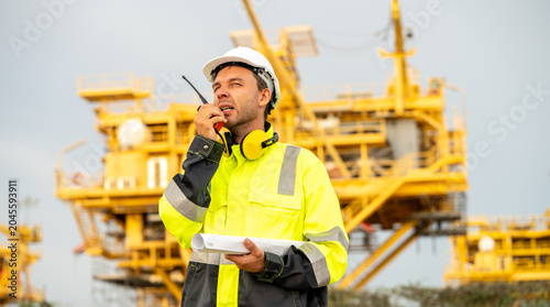 Cuadro en lienzo Industrial engineer using a walkie-talkie and holding a rolled blueprint at an offshore energy platform facility