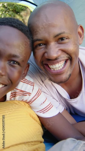 Vertical video: Cam starting, smiling dad and teen leaning in tent on mustard pillow, wearing tees