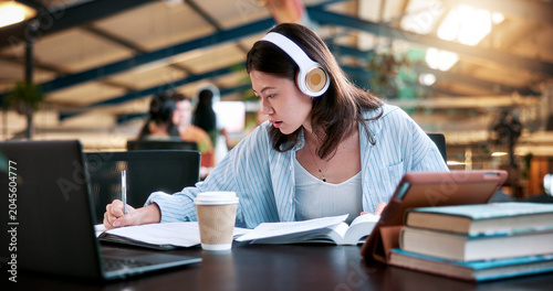 Tableau sur toile Woman, student and writing with headphones in library or university study for education or learning