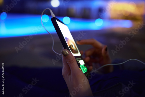 Woman using smartphone by pool at night – glowing screen, copy space, modern lifestyle