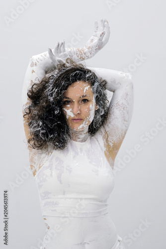 Portrait of a woman covered with white paint standing against a bright background with expressive pose intense gaze and artistic body textures creating a contemporary concept scene