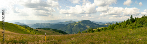 Mountain landscape panorama showing rolling green hills, lush valleys, scattered trees and dramatic cloud formations