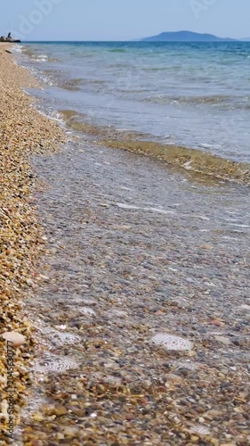 Pebble Beach With Clear Waves and Distant Island on a Calm Summer Day