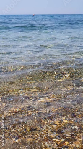 Pebble Beach With Clear Waves and Distant Island on a Calm Summer Day