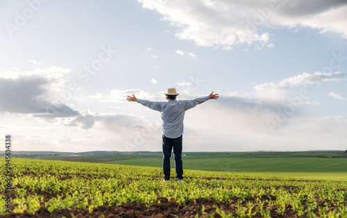 Foto Man in straw hat stands with arms outstretched in green agricultural field under