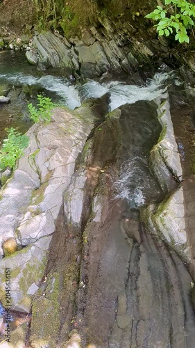 Tranquil Mossy Gorge With Small Waterfall Between Green Cliff Faces And Lush Plants