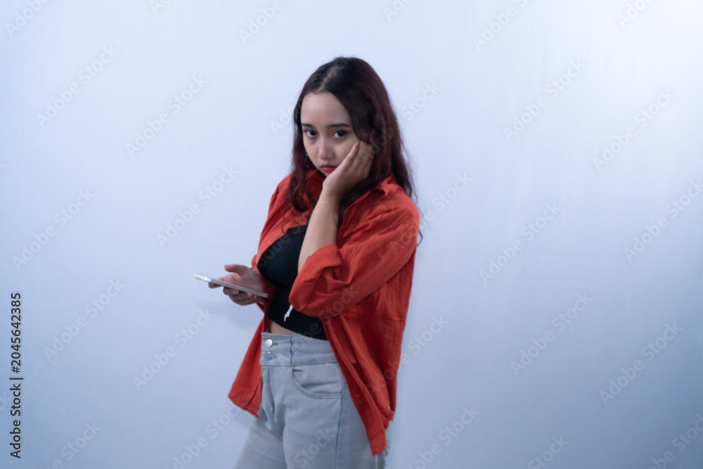 Naklejka premium Bored young woman holding smartphone and leaning face on hand on white background