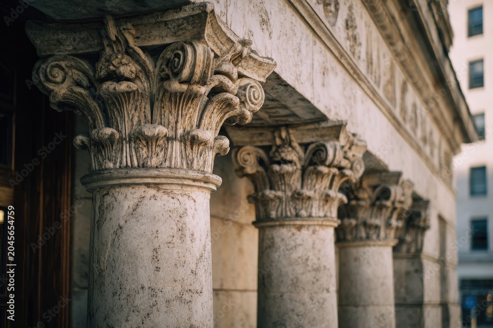 Fototapeta premium Four stone columns in a row on a civic education building facade, detailed capitals and weathered texture
