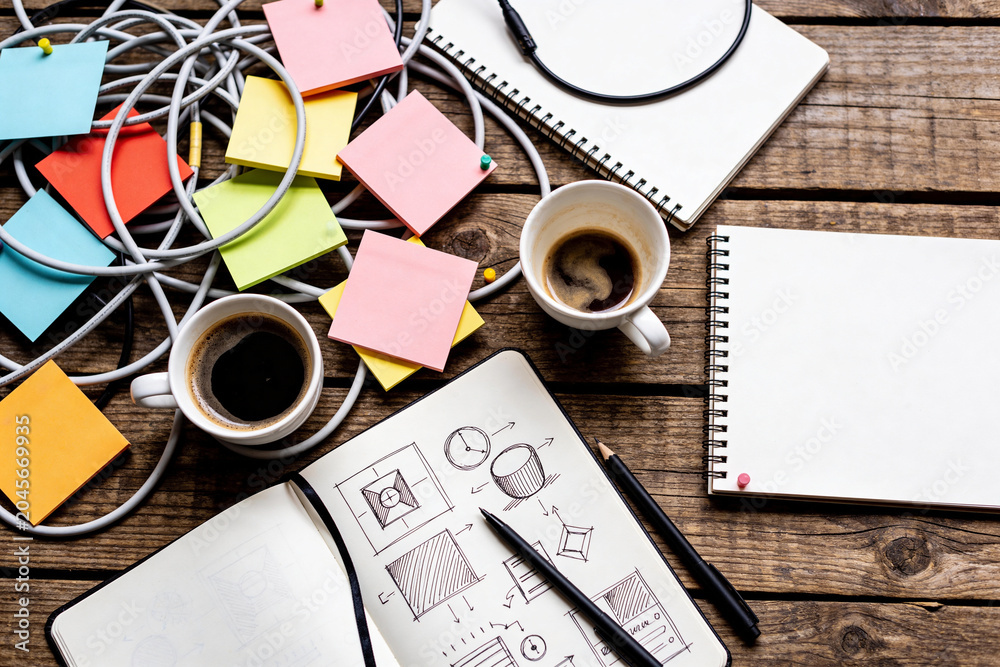Naklejka premium Messy creative brainstorm desk from above, sticky notes cables and coffee cups in an organic flat lay with copy space for text