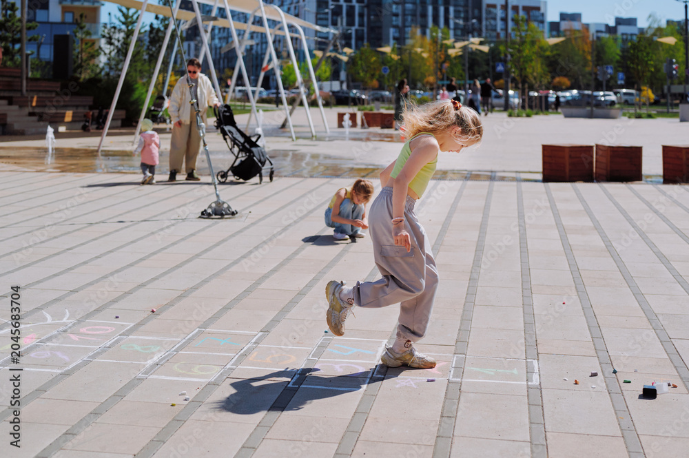 Obraz premium Young girls playing hopscotch on a sunny day in a contemporary city park.