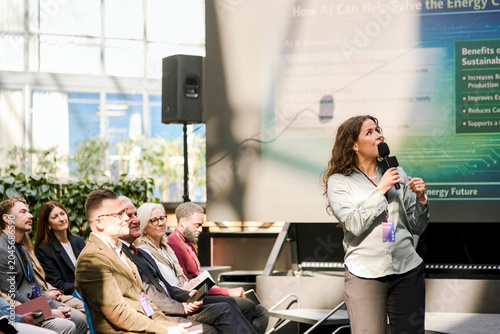 Mature female presenter discussing presentation points with audience while speaking into microphone during summit in con
