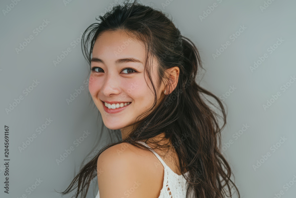 Fototapeta premium An attractive Asian woman poses in a white tank top with a bright smile, conveying health, happiness, and self care in an isolated setting.