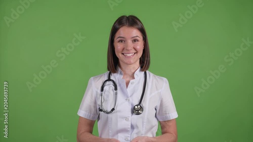 Confident young woman doctor in a white coat with a stethoscope speaking directly to the camera, providing medical advice on a green background