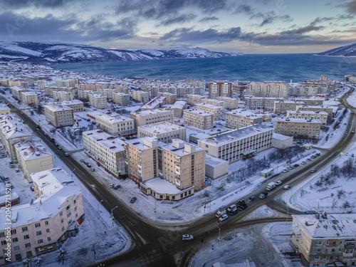 Schilderij op canvas Aerial winter view of snow-covered Magadan city with apartment blocks, roads and the icy Sea of Okhotsk against distant hills in the Russian Far East