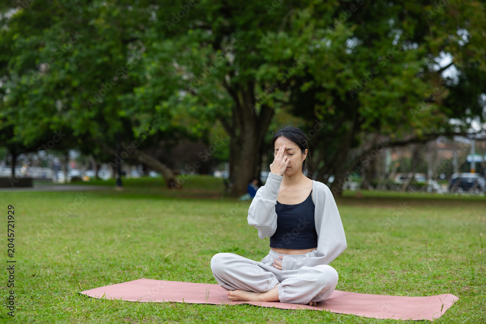Fototapeta premium Young woman practicing alternate nostril breathing yoga in park