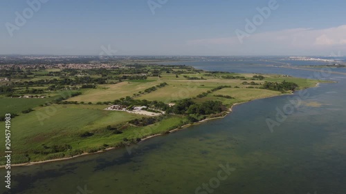 Aerial view of green coastal farmland and lagoon under blue sky in southern France