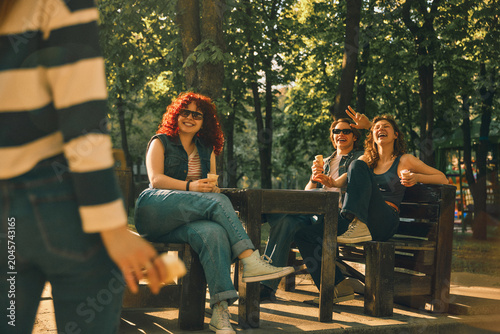 Canvas-taulu Friends relaxing at park table and greeting newcomer with vintage effect