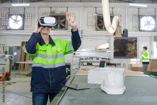 Fotografía Happy female engineer in safety clothes holds wears virtual reality device glasses at industry plant