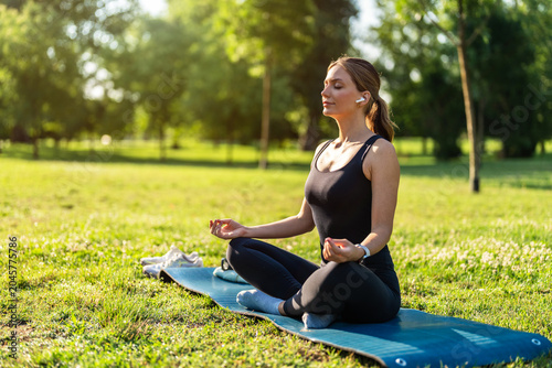 Yoga, young woman meditation in park with lotus pose, earphone for mindfulness podcast and zen outdoor in nature. Peace, spiritual energy and balance self care and music with fitness and wellness