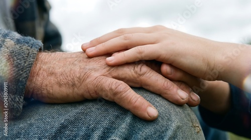 A young hand rests on an older wrinkled hand showing care and connection