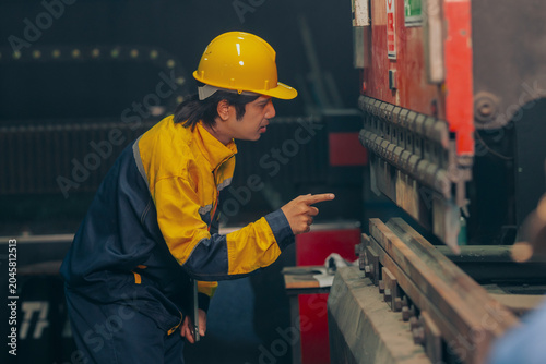 Obraz na płótnie Group of diverse Asian technicians and female industry specialists collaborating next to production machinery, checking maintenance checklists and auditing plant operations to ensure workplace safety