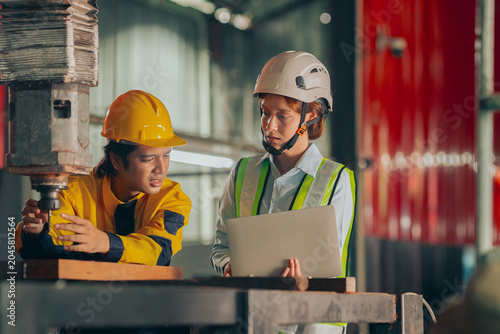 Schilderij op canvas Group of diverse Asian technicians and female industry specialists collaborating next to production machinery, checking maintenance checklists and auditing plant operations to ensure workplace safety