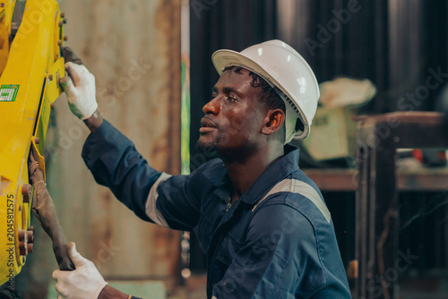 Foto Professional technician in a hardhat operating a portable computer to configure and maintain a yellow industrial robot machinery inside a modern manufacturing plant, focusing on Industry 4