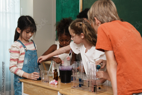 A group of multi-ethnic school children pouring liquids and mixing colorful chemicals in test tubes, enjoying a hands-on STEM education class and interactive teamwork activity.