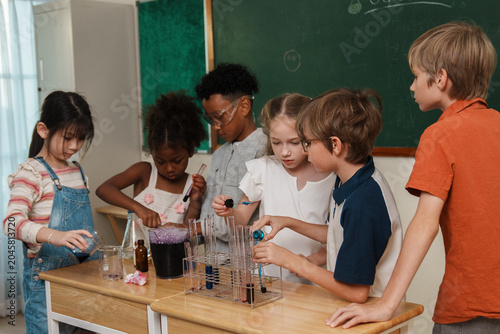 A group of multi-ethnic school children pouring liquids and mixing colorful chemicals in test tubes, enjoying a hands-on STEM education class and interactive teamwork activity.