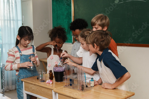 A group of multi-ethnic school children pouring liquids and mixing colorful chemicals in test tubes, enjoying a hands-on STEM education class and interactive teamwork activity.