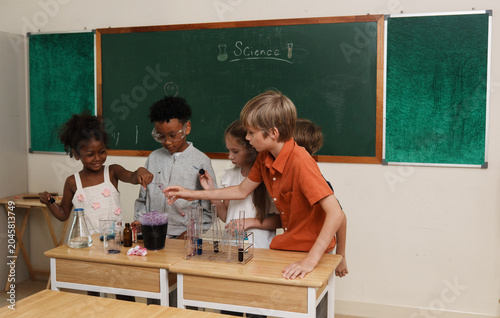A group of multi-ethnic school children pouring liquids and mixing colorful chemicals in test tubes, enjoying a hands-on STEM education class and interactive teamwork activity.
