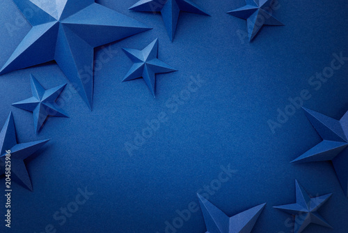 Monochrome blue composition with folded paper stars arranged around the edges on a dark blue background. Patriotic border with empty space for text, suitable for Independence, Fourth of July, Memorial