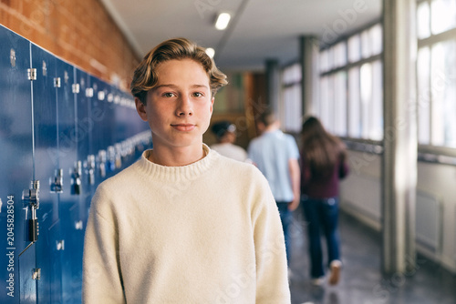 Portrait of junior high male student standing near locker in school lobby
