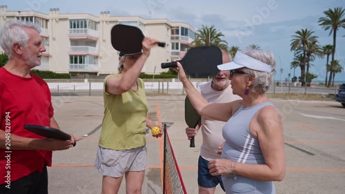 Four senior friends playing pickleball outdoors