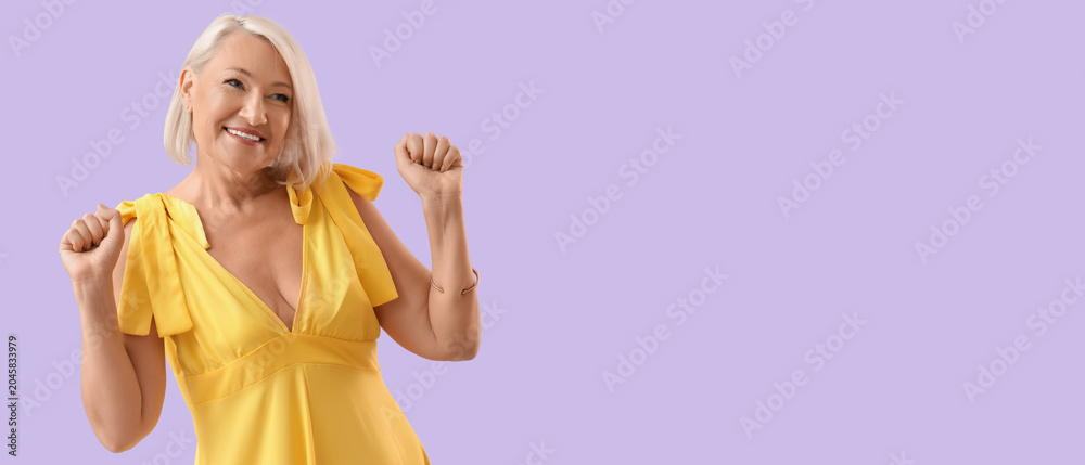 Obraz premium Beautiful mature woman in yellow dress dancing on lilac background