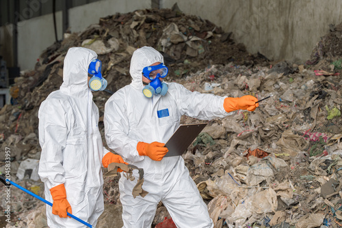 Waste Management Professionals Pointing and Discussing Site Operation: Experts in hazmat suits analyze and discuss findings at a recycling facility, emphasizing careful site management, safety.