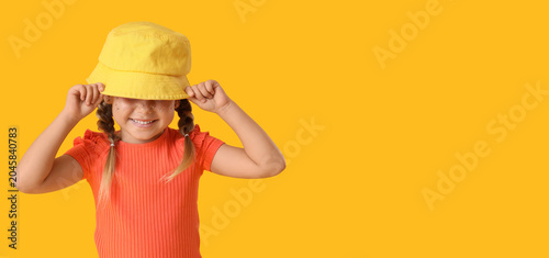 Stylish little girl in bucket hat on yellow background