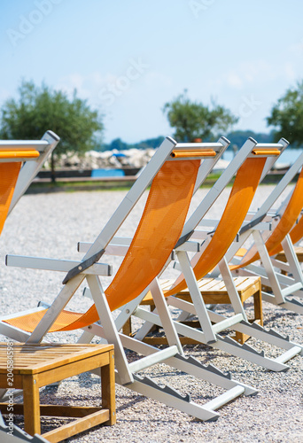 Cuadro en lienzo Orange sun loungers arranged on beach with lake view, summer vacation atmosphere