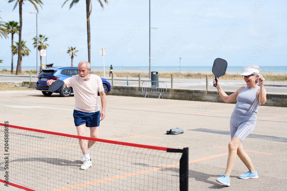 Obraz premium Active senior couple playing pickleball outdoors