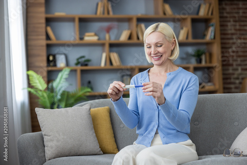 Bilde på lerret Smiling mature woman holding a positive pregnancy test, embracing the news of un