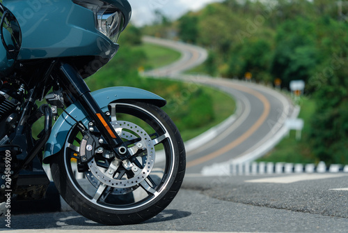 Sleek motorcycle with shiny front wheel parked on scenic winding road, surrounded by lush greenery