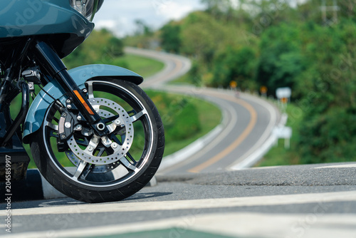 Sleek motorcycle with shiny front wheel is parked on scenic road, surrounded by lush greenery and winding path ahead