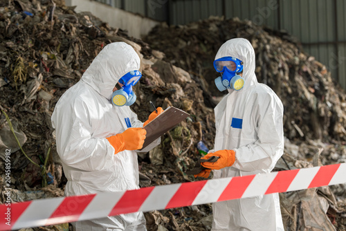 Fotografie Hazardous Waste Management Inspection:Dedicated professionals in full protective gear inspect waste at a large-scale recycling, disposal facility